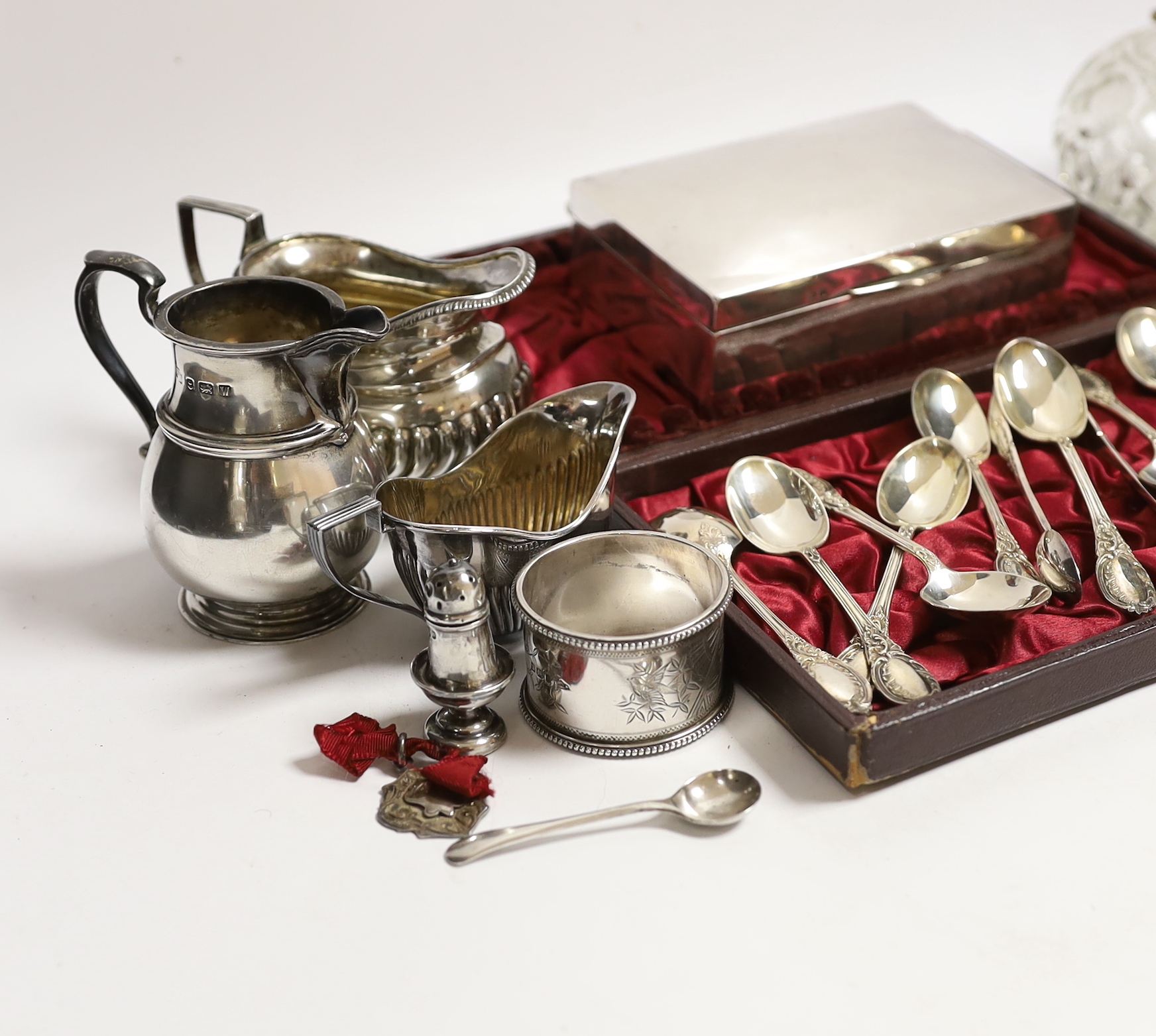 A Victorian silver mustard pot (no liner), a cased set of twelve silver teaspoons and tongs, two silver cream jugs, mounted glass scent bottle, napkin rings etc.